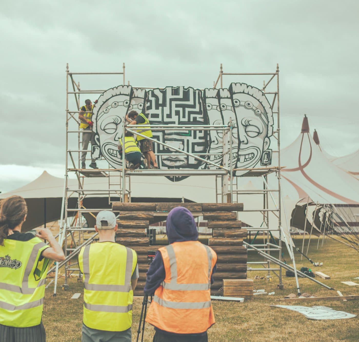 Volunteers building the festival site in daylight, carrying scaffold and timber.
