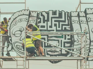 Crew on scaffolding painting the carved-faces mural of The Maw